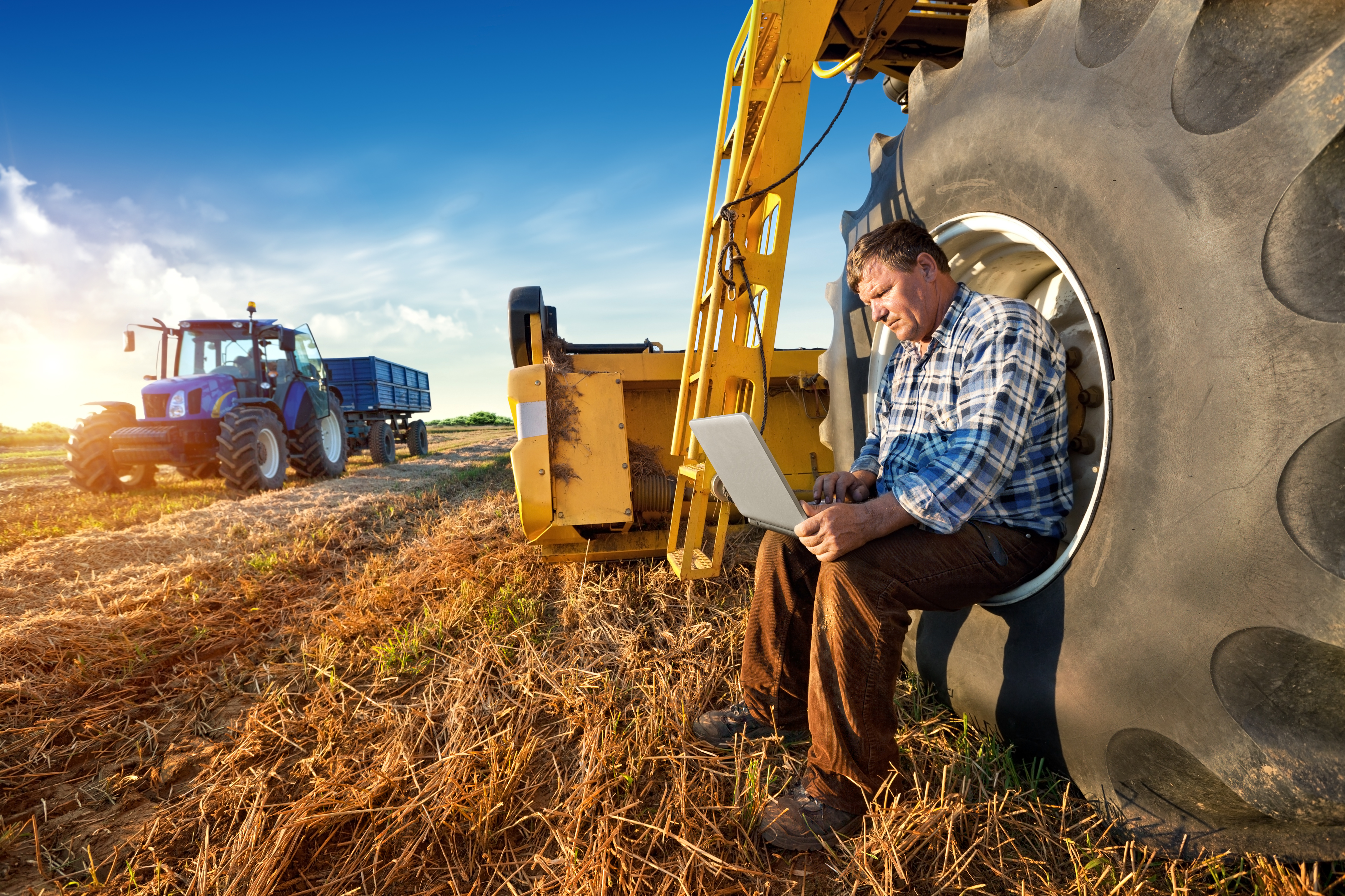 Ein Landwirt sitzt mit seinem Laptop an einem Traktor auf dem Feld.