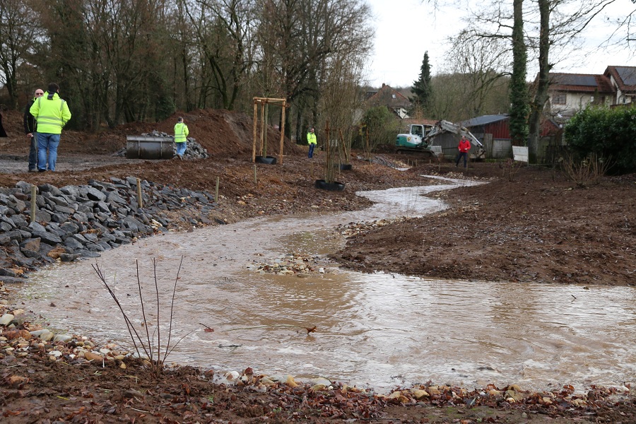 Ein Bach windet sich durch eine Baustelle. Am Rand werden Steine verlegt und es ist viel Erde zu sehen.