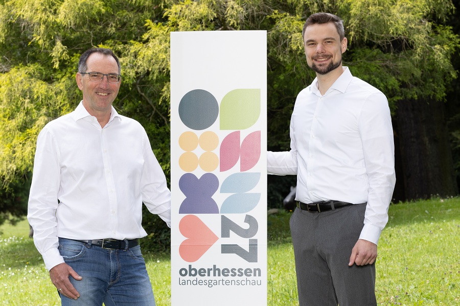 An einer Stele lehnen links und rechts die Geschäftsführer.