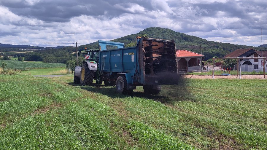 Landwirtschaftlicher Lastzug verteilt Pflanzenkohle auf einem bewachsenen Acker.