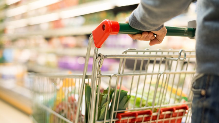Eine Person schiebt einen Einkaufswagen durch einen Supermarkt.